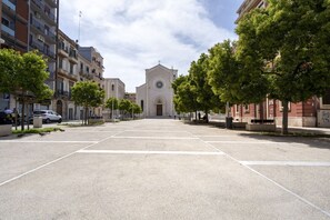 A street leading to a church with a clock tower, surrounded by multi-story buildings and trees.