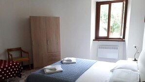 Quarto com cama, guarda-roupa, cadeira, janela e radiador.