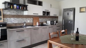 Uma cozinha moderna com armários cinza, uma geladeira de aço inoxidável e uma área de jantar com mesa e cadeiras de madeira.