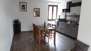 Uma sala de jantar com mesa e cadeiras de madeira, uma cozinha com armários e eletrodomésticos, e uma janela que oferece iluminação natural.