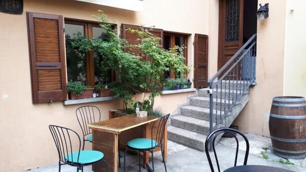 Pequeno pátio exterior com mesa e cadeiras de madeira, escadas e um barril.