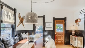 A dining area with a long wooden table, black and white checkered cushions, a woven pendant light, and a white dog.