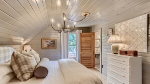 A bedroom with a bed, pillows, a dresser, a lamp, and a window with curtains.