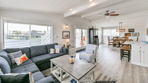 Ein geräumiges Wohnzimmer mit einem grauen Ecksofa, einem Couchtisch und einem Essbereich mit Holztisch und Stühlen.