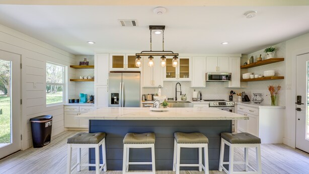 A modern kitchen with a large island, white cabinetry, and bar stools.