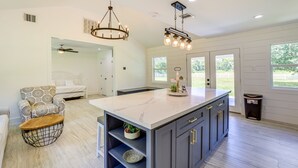 A modern kitchen with a marble island, dark cabinets, and pendant lighting.