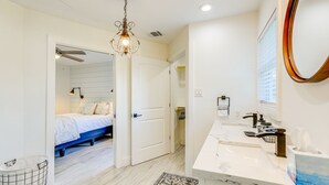 A bedroom with a bed, a bathroom with a sink and mirror, and a hallway with a door leading to another room.