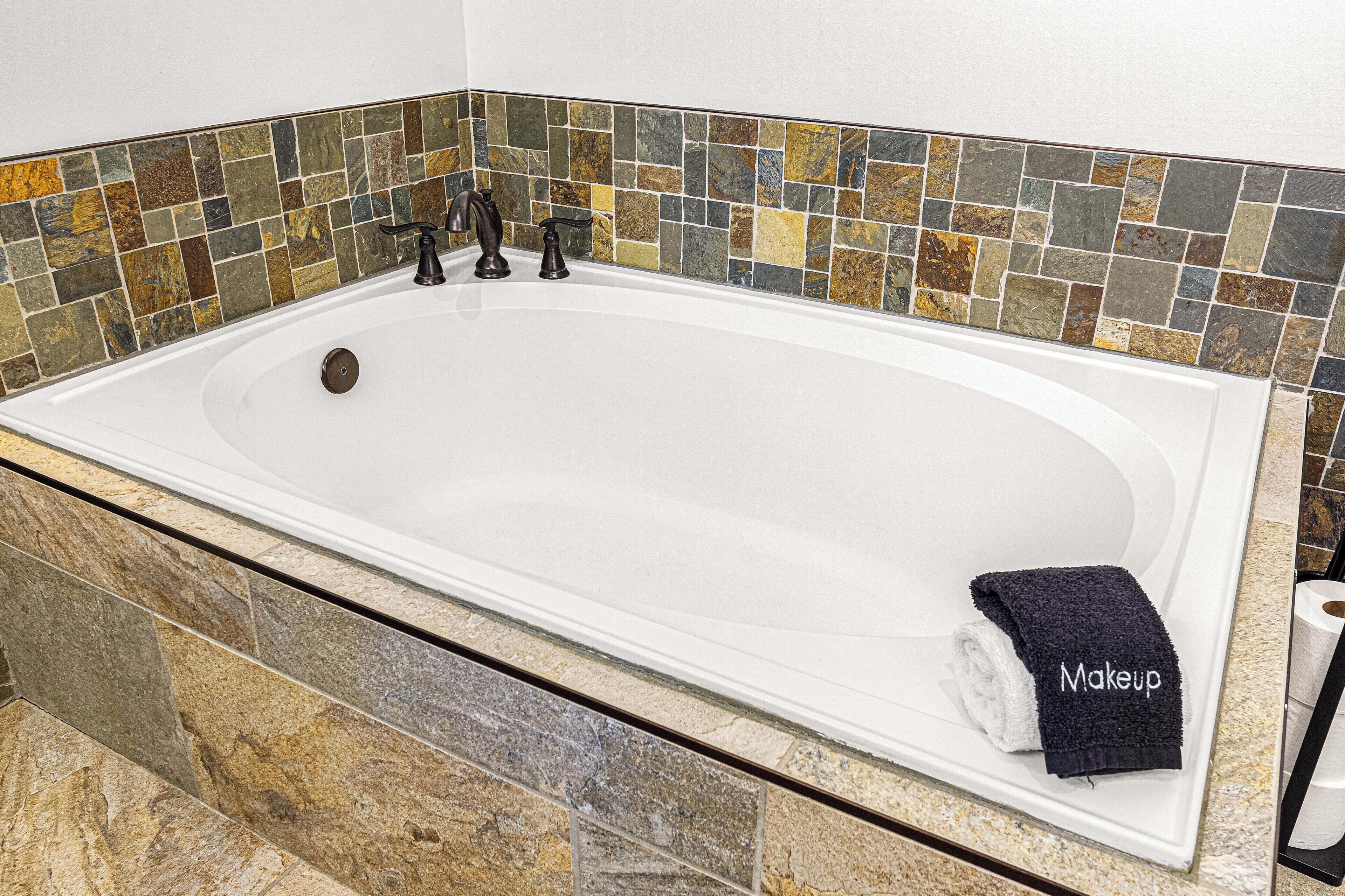 A bathtub with a mosaic tile wall, a towel, and a bottle of shampoo.