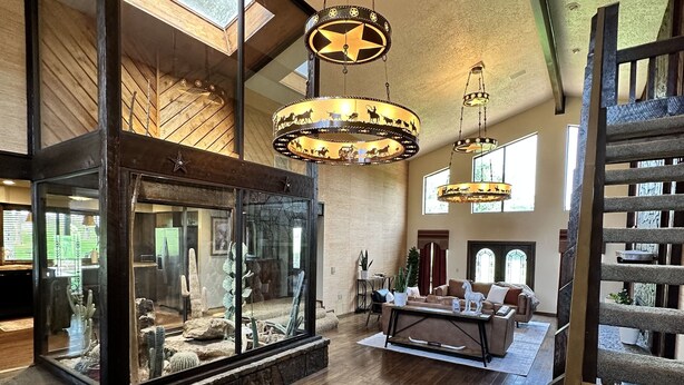 A spacious living area with a glass enclosure displaying cacti, a wooden staircase, and a large chandelier. - 1980s Rustic Ranch house is the Perfect Place for events at the Lazy E. (Guthrie)