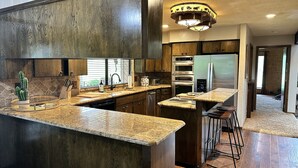 A modern kitchen with dark wood cabinets, granite countertops, stainless steel appliances, and a central island with bar stools. - 1980s Rustic Ranch house is the Perfect Place for events at the Lazy E. (Guthrie)