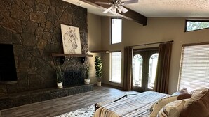 A bedroom with a stone fireplace, a bed with striped bedding, a patterned rug, and a ceiling fan. - 1980s Rustic Ranch house is the Perfect Place for events at the Lazy E. (Guthrie)