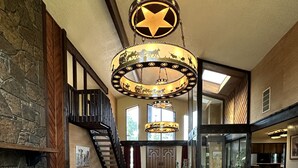 A spacious living area with a large brown leather sofa, a fireplace, and a chandelier. - 1980s Rustic Ranch house is the Perfect Place for events at the Lazy E. (Guthrie)