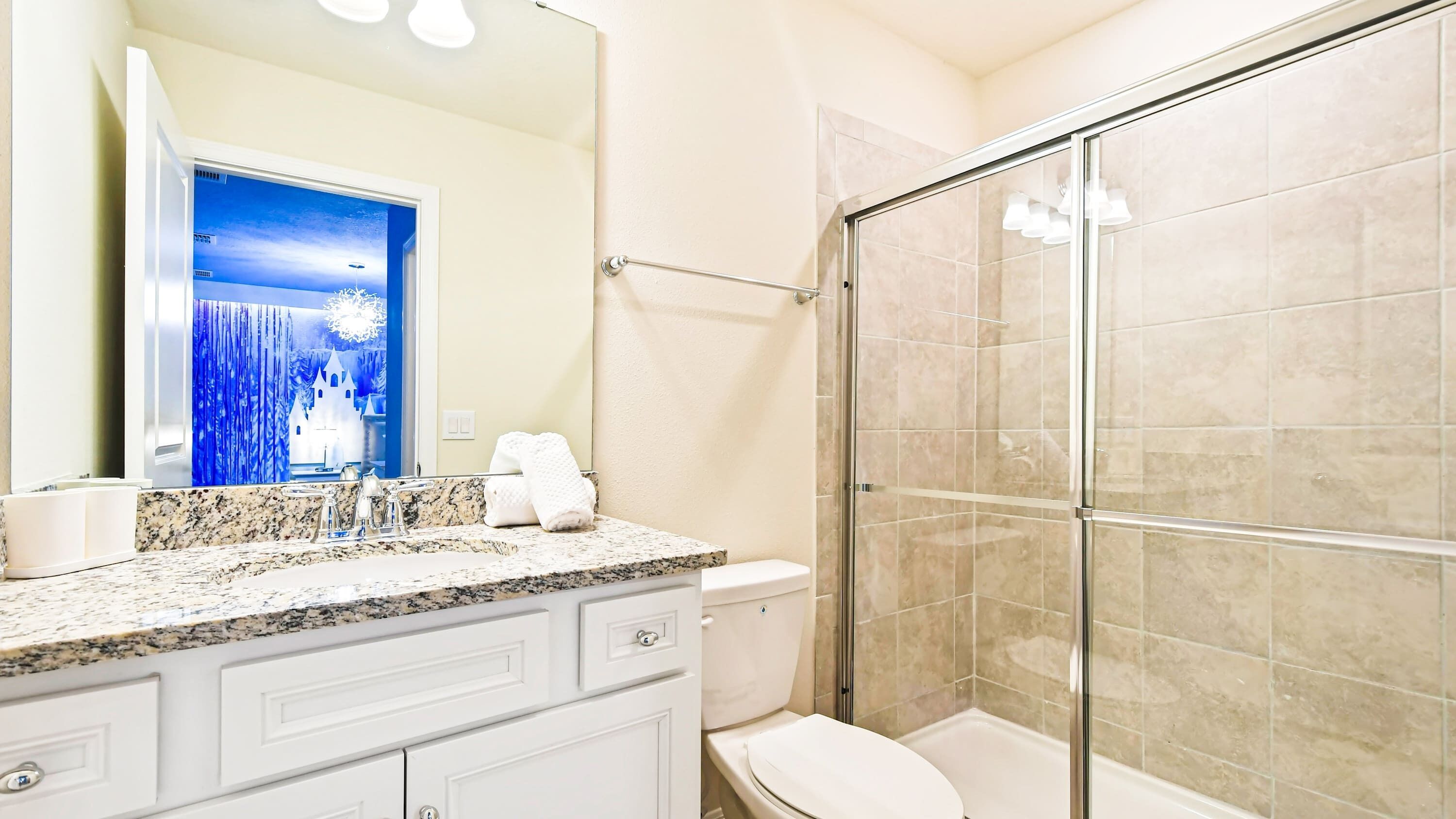A bathroom with a granite countertop, a toilet, a glass shower enclosure, and a large mirror with a decorative scene.