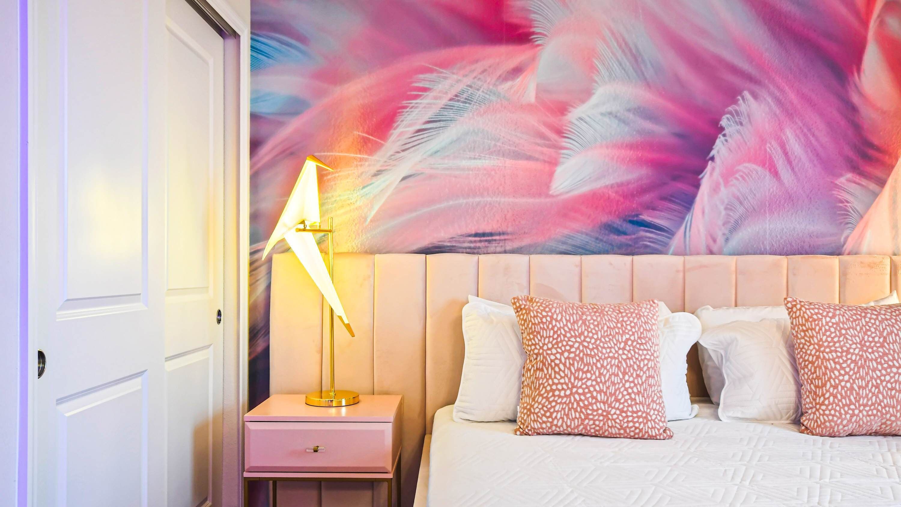 A bedroom with a bed, a nightstand, a lamp, and a wall mural.