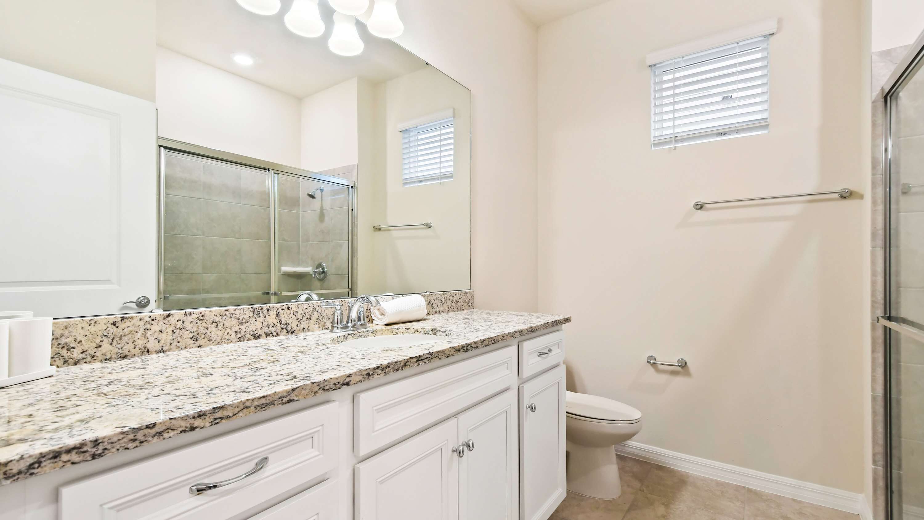 Une salle de bain dotée d’un comptoir en granit, d’un grand miroir, de toilettes et d’une cabine de douche.