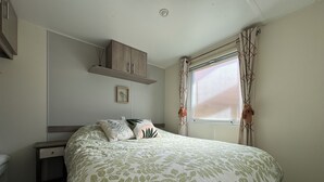 Une chambre à coucher avec un lit, une table de chevet, une étagère au-dessus du lit, une fenêtre avec des rideaux et un tableau encadré au mur.