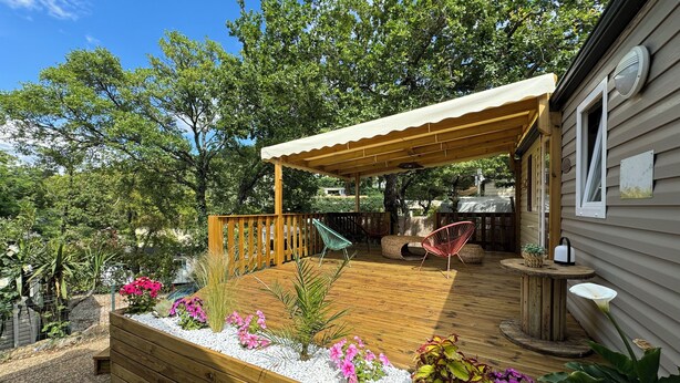 Une terrasse en bois agrémentée d’une pergola, entourée de galets blancs et de fleurs aux couleurs vives.