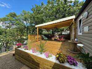 Une terrasse en bois agrémentée d’une pergola, entourée de galets blancs et de fleurs aux couleurs vives.