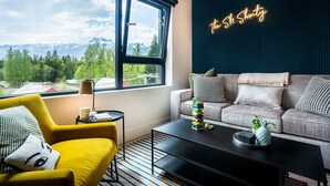A modern living room with a view of mountains, a neon sign, a sofa, a coffee table, and a yellow armchair. - The Ski Shanty by Revelstoke Vacations (Revelstoke)