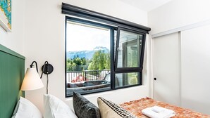 A hotel room with a bed, a window with a view of mountains, a lamp, and a door. - The Ski Shanty by Revelstoke Vacations (Revelstoke)