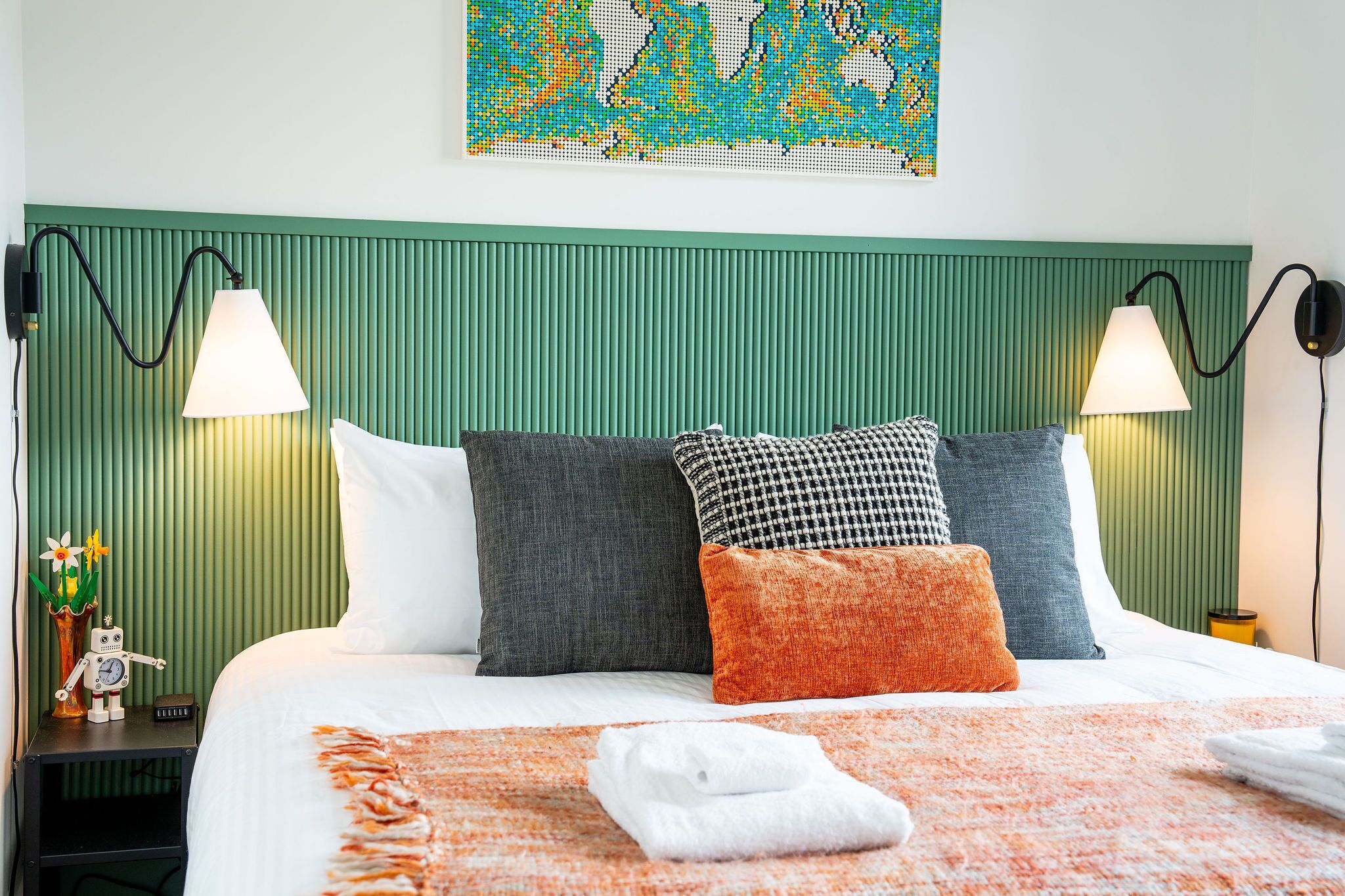A neatly made bed with pillows, a blanket, and a folded towel. There are two wall-mounted lamps on either side of the bed.
