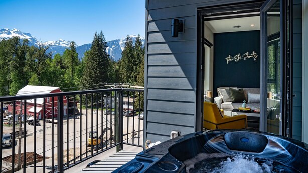 A modern hotel room with a balcony overlooking a mountain view, a hot tub, and a cozy seating area. - The Ski Shanty by Revelstoke Vacations (Revelstoke)
