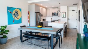 A modern kitchen with white cabinets, a stainless steel refrigerator, and a microwave. There is a dining table with benches and a potted plant. - The Ski Shanty by Revelstoke Vacations (Revelstoke)