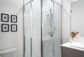 Un baño moderno con ducha de vidrio, inodoro y lavamanos con espejo.