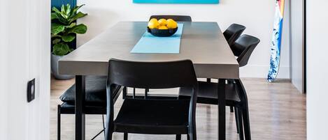 A modern dining area with a wooden table, black chairs, a blue abstract painting, and a ski on the wall.