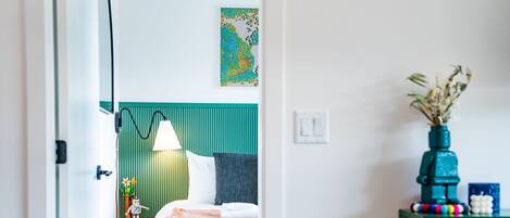 Una habitación de hotel moderna con una cama, una mesita de noche, una lámpara, una obra de arte en la pared y un florero con flores secas.