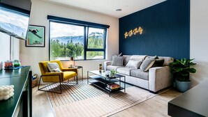 A modern living room with a sofa, a yellow armchair, a coffee table, and a large window offering a mountain view. - The Ski Shanty by Revelstoke Vacations (Revelstoke)