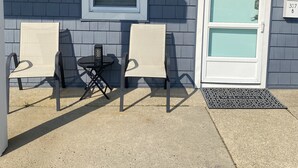 Een huis met een blauwe gevel, een witte deur met een krans, en twee stoelen ervoor.