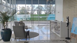 A spacious lobby with a reception desk, a large potted plant, and a seating area with a round table and chairs.