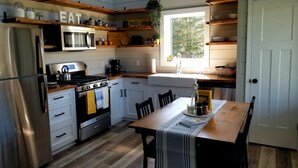 Una cocina con estantes de madera, un refrigerador, una estufa y una ventana que proporciona luz natural.