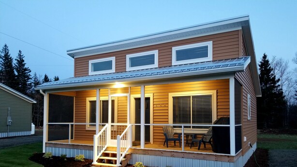 Una casa de dos pisos con un porche cubierto, una escalera que conduce a la entrada y un pequeño patio con mobiliario de exterior.