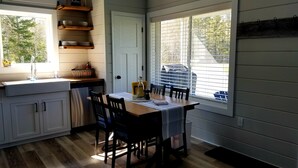 Una cocina con armarios de madera, una mesa de comedor con sillas, una ventana con persianas y una puerta.