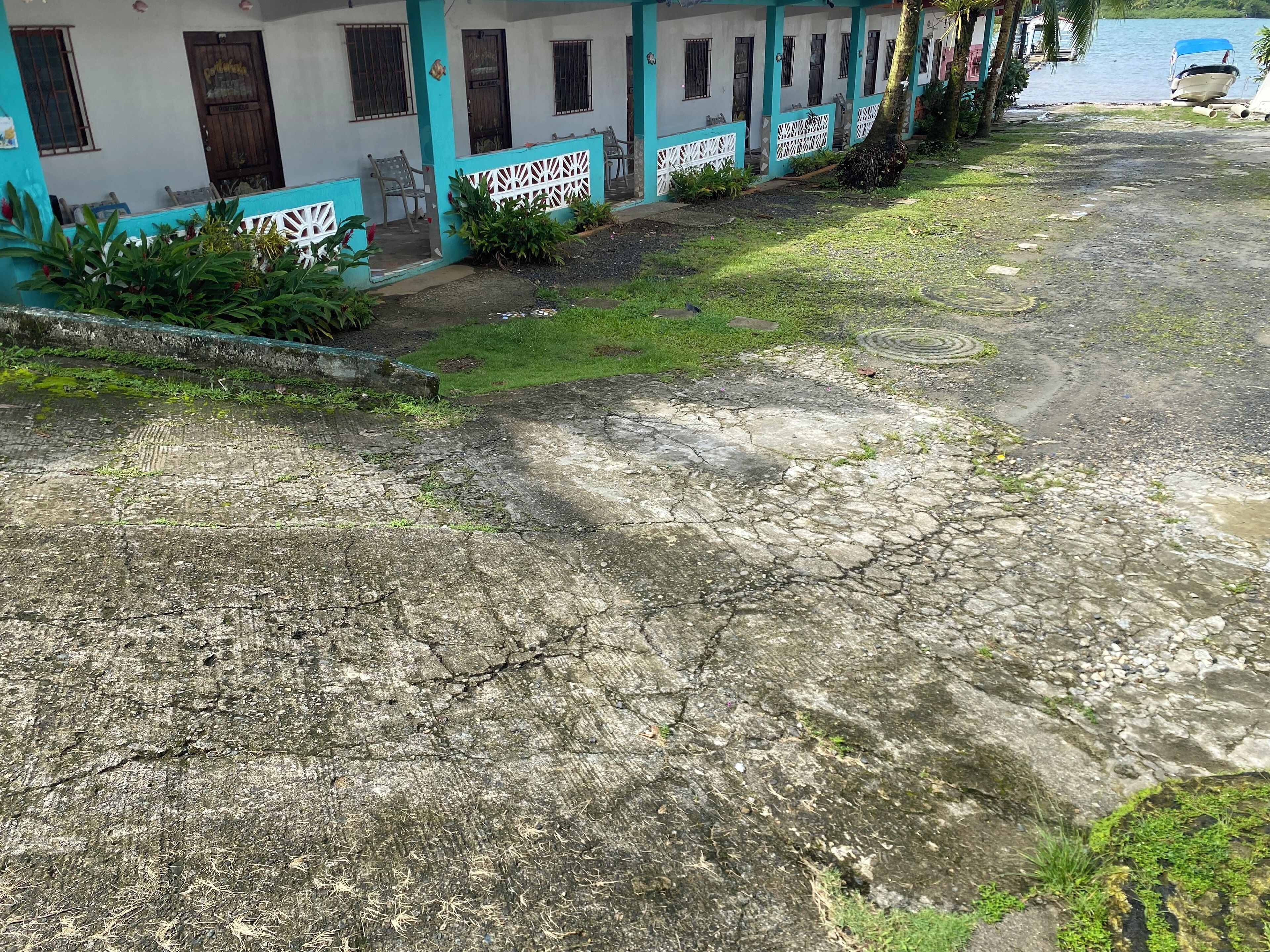 Una hilera de edificios blancos y turquesas con una carretera dañada y agrietada al frente.
