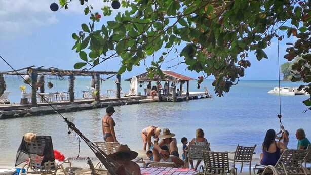 A beachside setting with a dock, lounge chairs, and a table under a tree. - Villa Bella Portobelo (Portobelo)