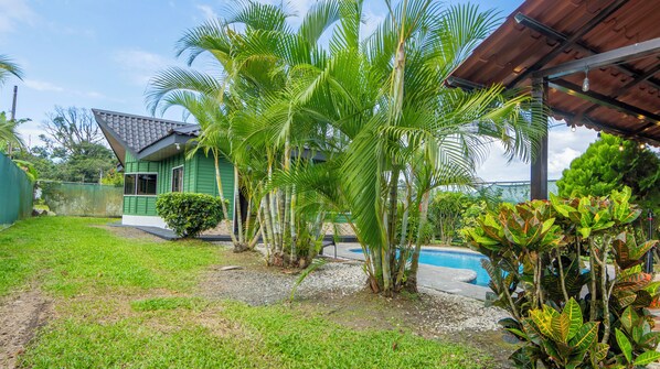 A green house with a swimming pool, surrounded by lush greenery and palm trees.