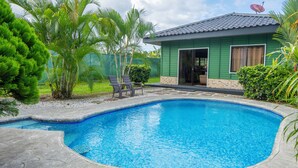 A swimming pool with a tiled edge, surrounded by a patio area with chairs and a small building with a green exterior. - Sweet home, La Fortuna/ private pool / free concierge / 5 minutes from downtown (La Fortuna)