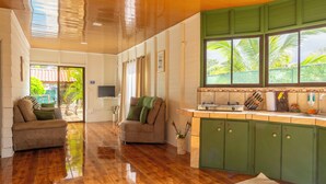 A spacious living area with a wooden floor, two sofas, a TV, and a kitchen with green cabinets and a window overlooking greenery. - Sweet home, La Fortuna/ private pool / free concierge / 5 minutes from downtown (La Fortuna)