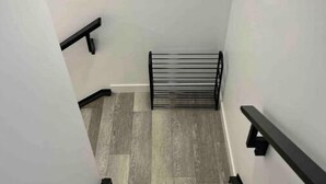 Un escalier avec des marches en bois et des rampes noires, menant à un palier sur lequel se trouve un présentoir en métal.