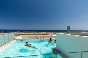 Une piscine à l’eau d’un bleu cristallin, avec une barrière en verre et une vue sur l’océan.