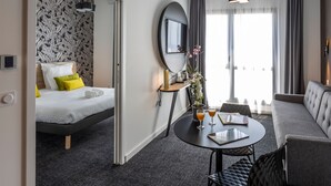 Ein Hotelzimmer mit Bett, Sofa, rundem Tisch mit Getränken, Spiegel und Fenster mit Vorhängen.