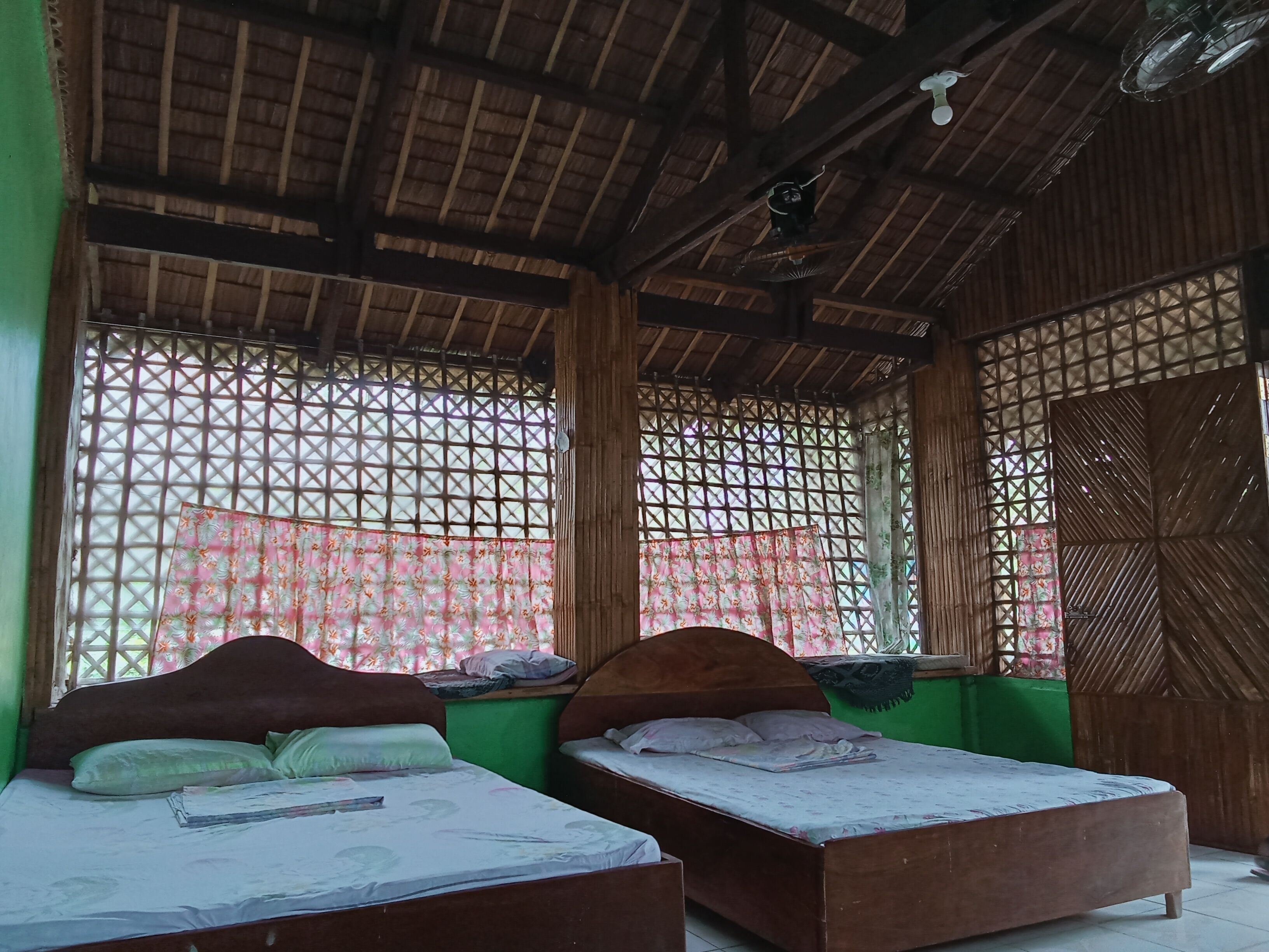 A room with two wooden beds, a thatched roof, and a lattice window.