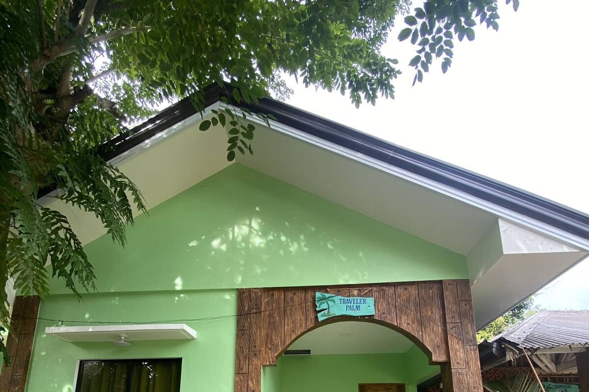 A green building with a wooden archway labeled "Traveler Palm."