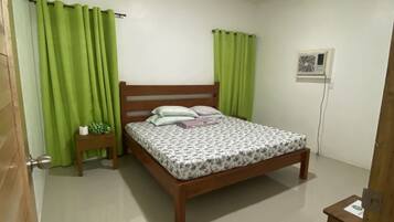 Un dormitorio con una cama de madera, cortinas verdes, una mesita de noche pequeña y un aire acondicionado instalado en la pared.
