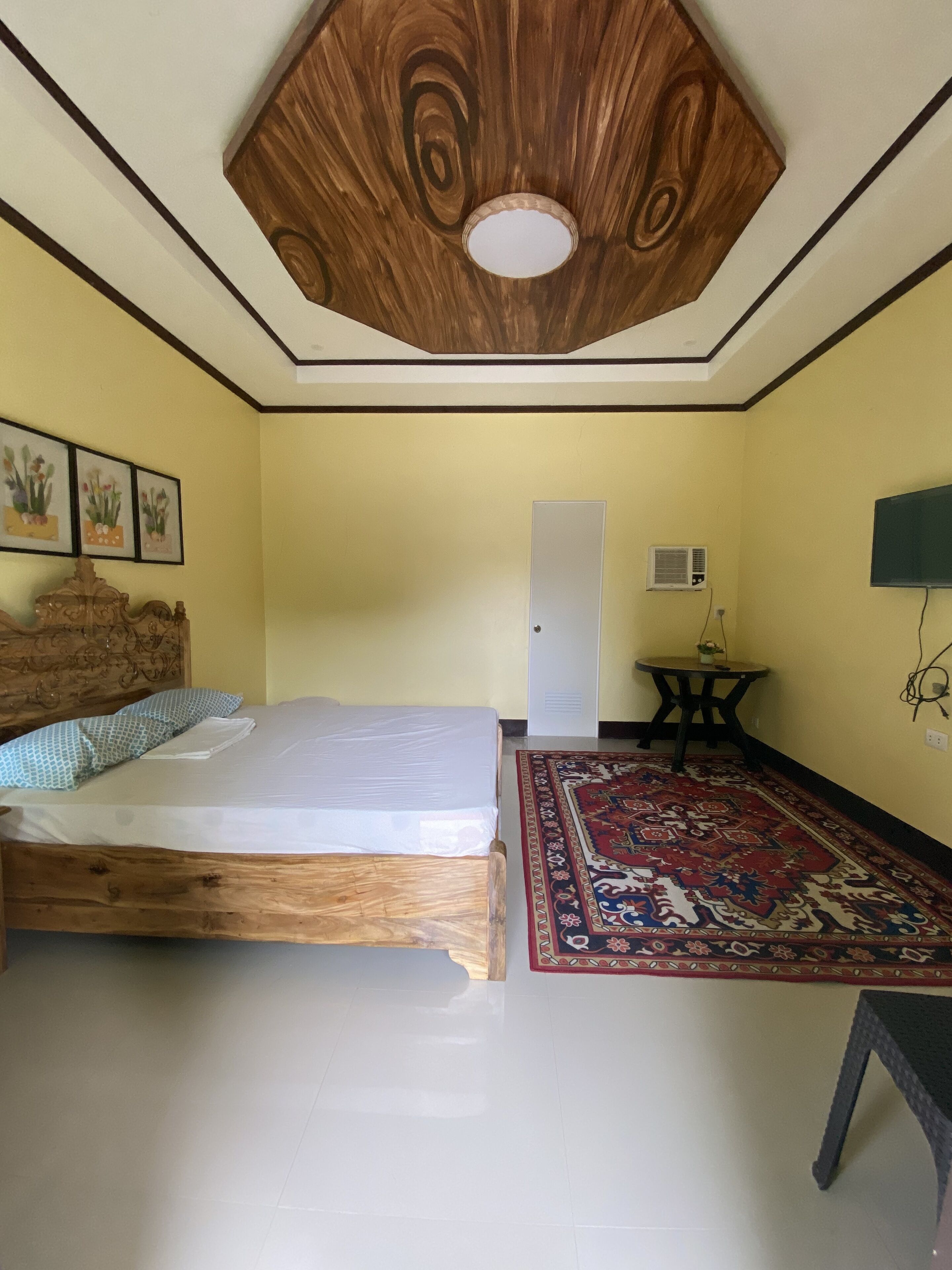 Une chambre à coucher avec un lit en bois, un tapis à motifs, une petite table et un plafond orné de motifs en bois.