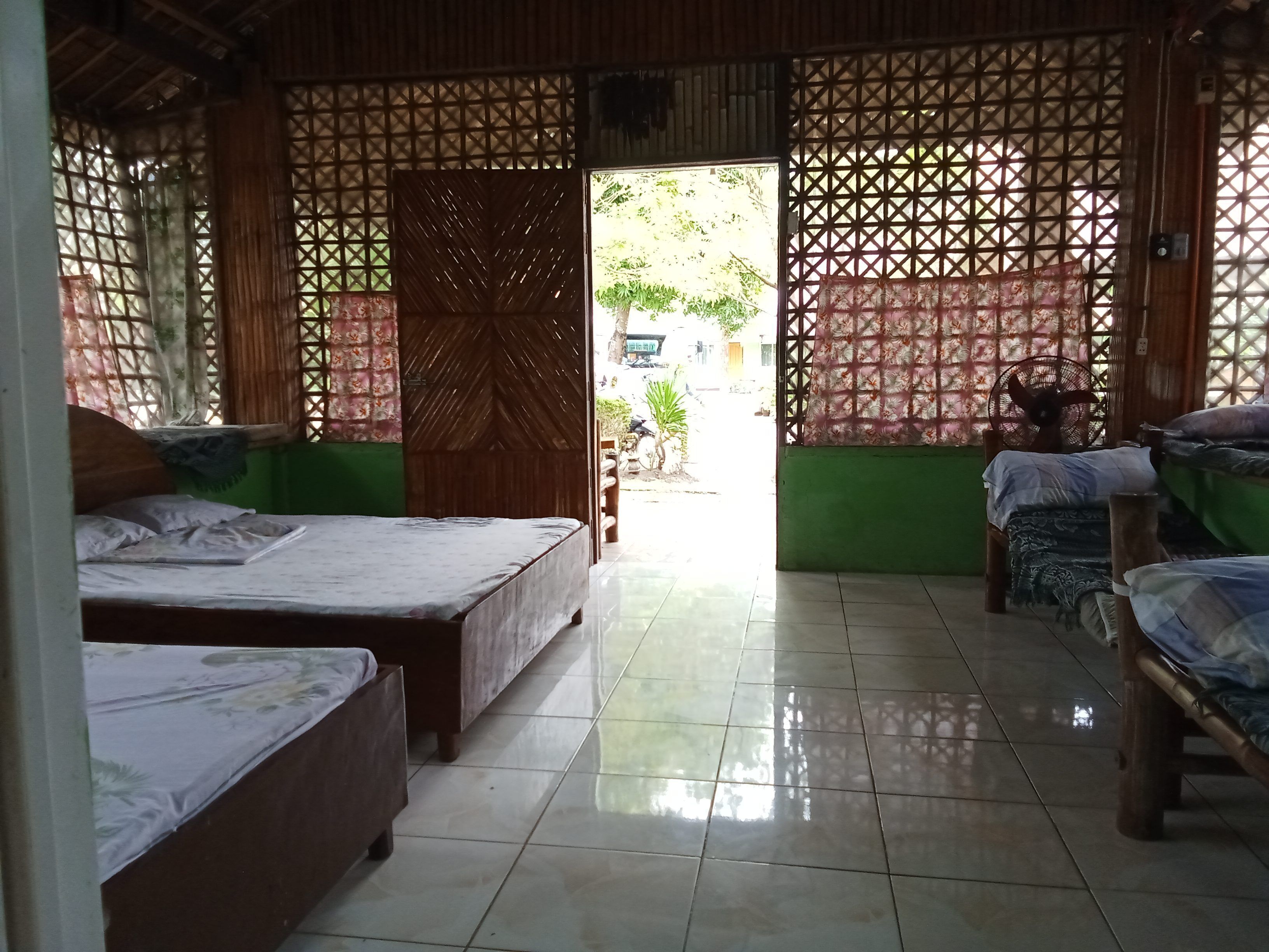 A room with two beds, a wooden door, and a tiled floor.