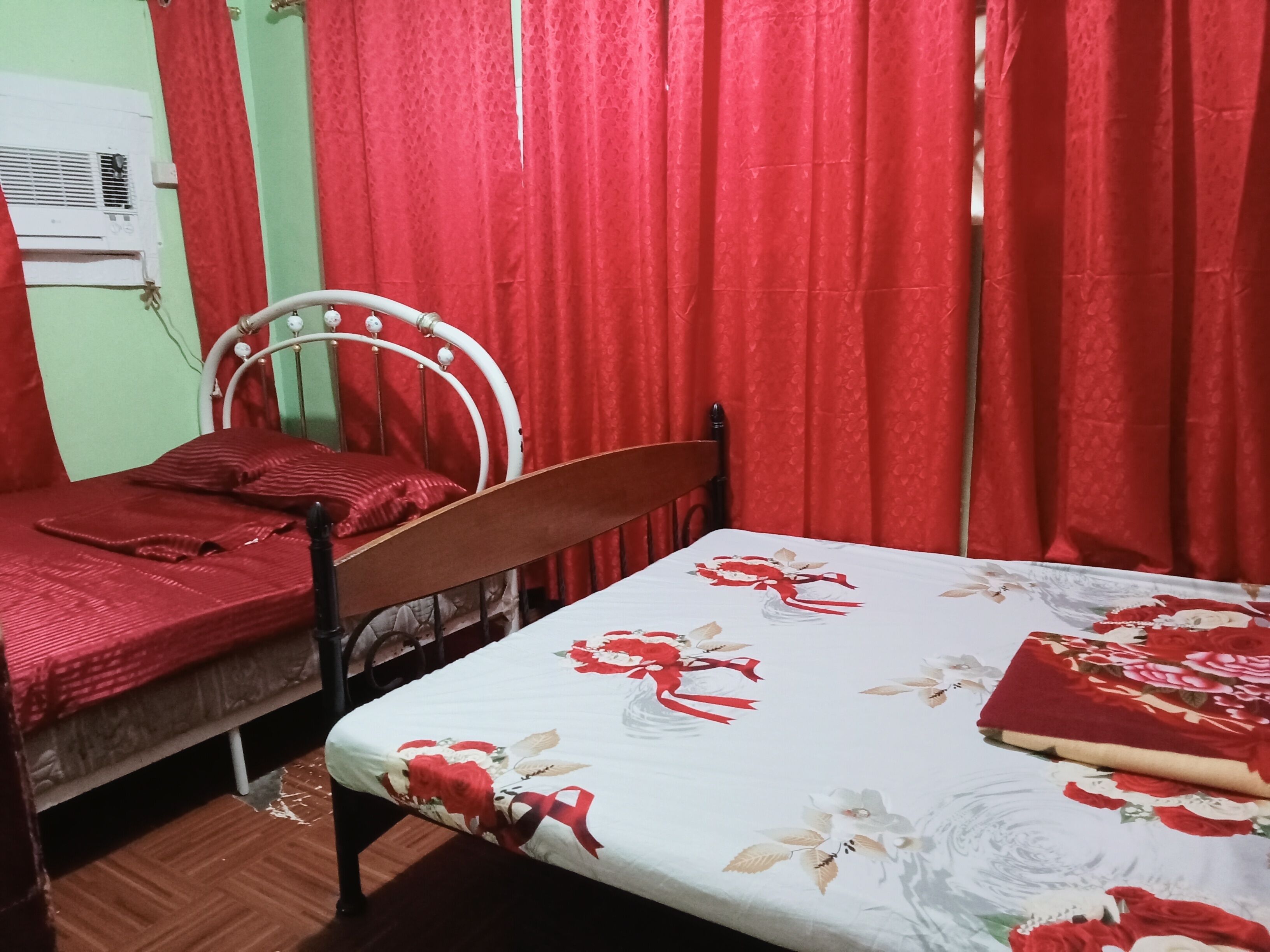 A room with two single beds, red curtains, a white air conditioner, and a floral bedspread.